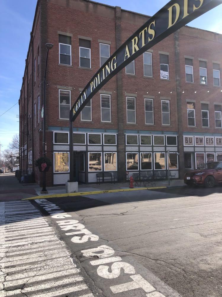The brick building in daylight, under the arched Kelly Poling Arts District sign