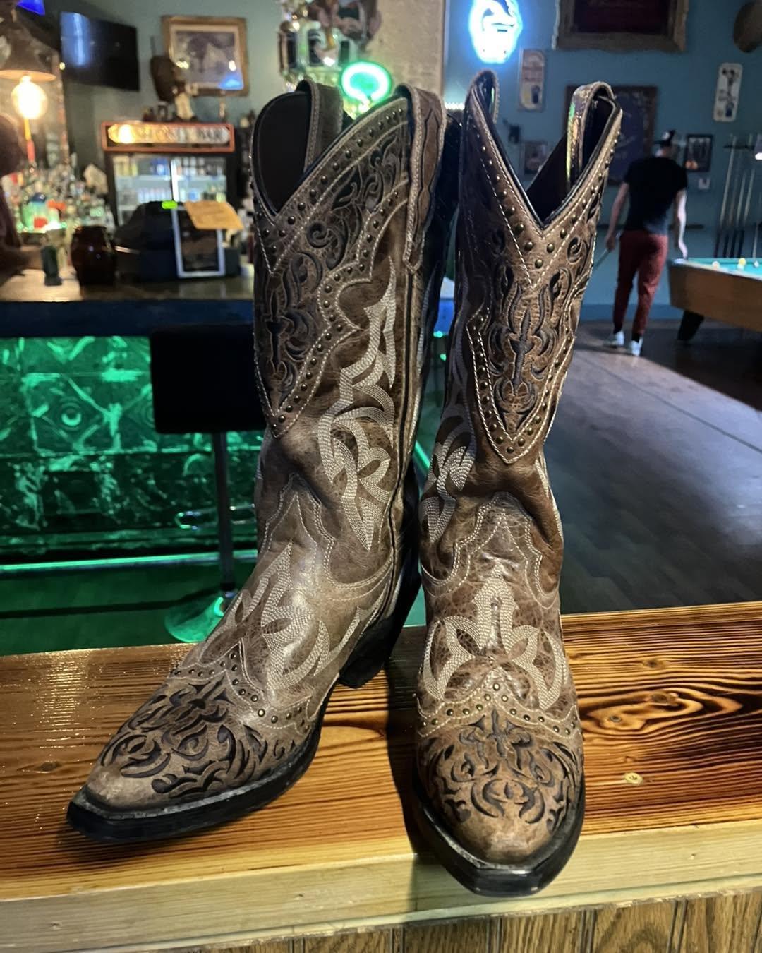 A pair of tooled cowboy boots on the torched-wood bar top, the pool table behind