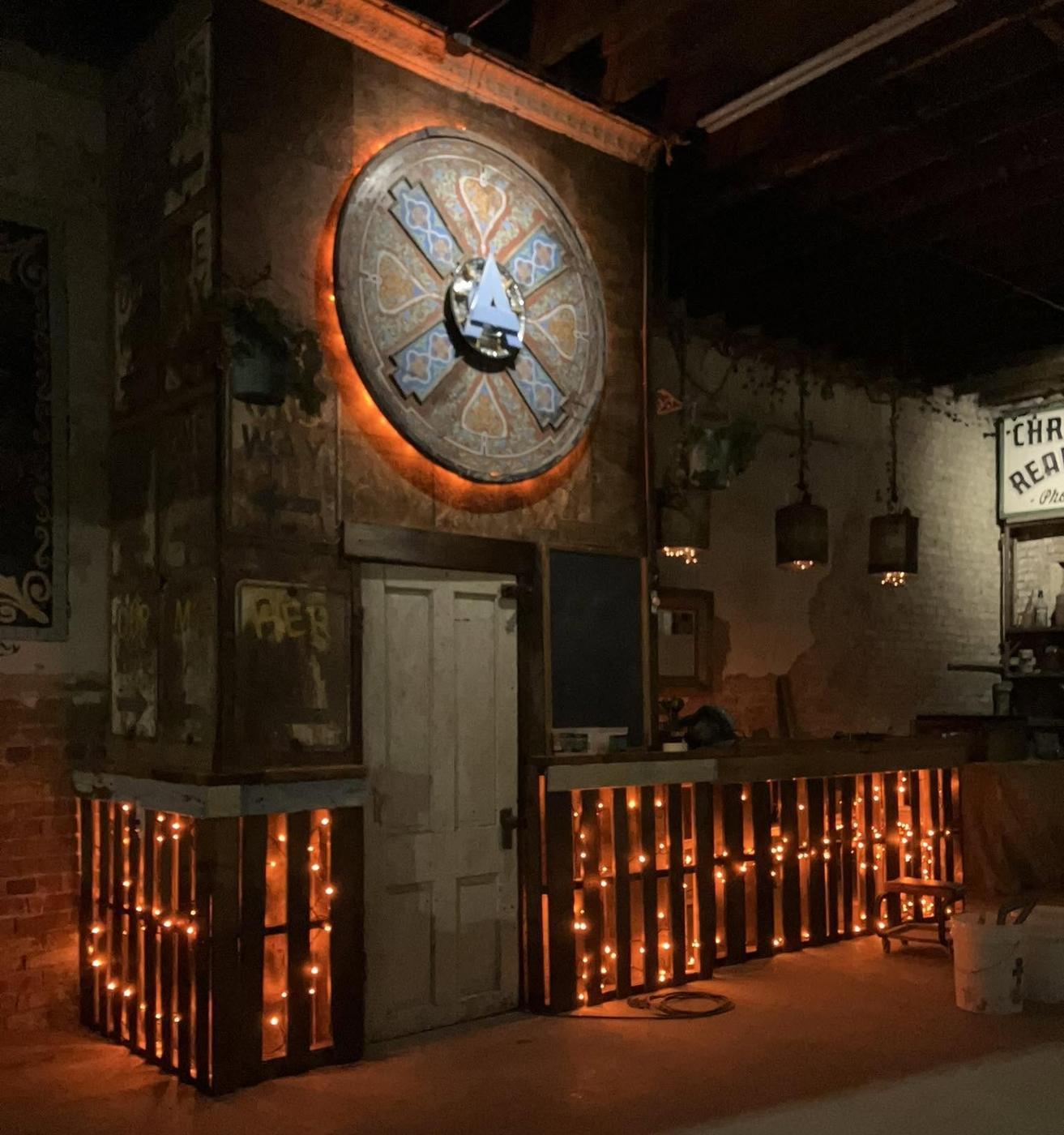 The Brickyard room: exposed brick, a lit circular medallion on the back wall and a pallet-board bar front strung with warm lights